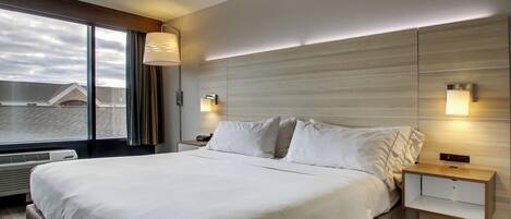 A hotel room with a large bed, bedside tables, a window with curtains, and a view of buildings outside.