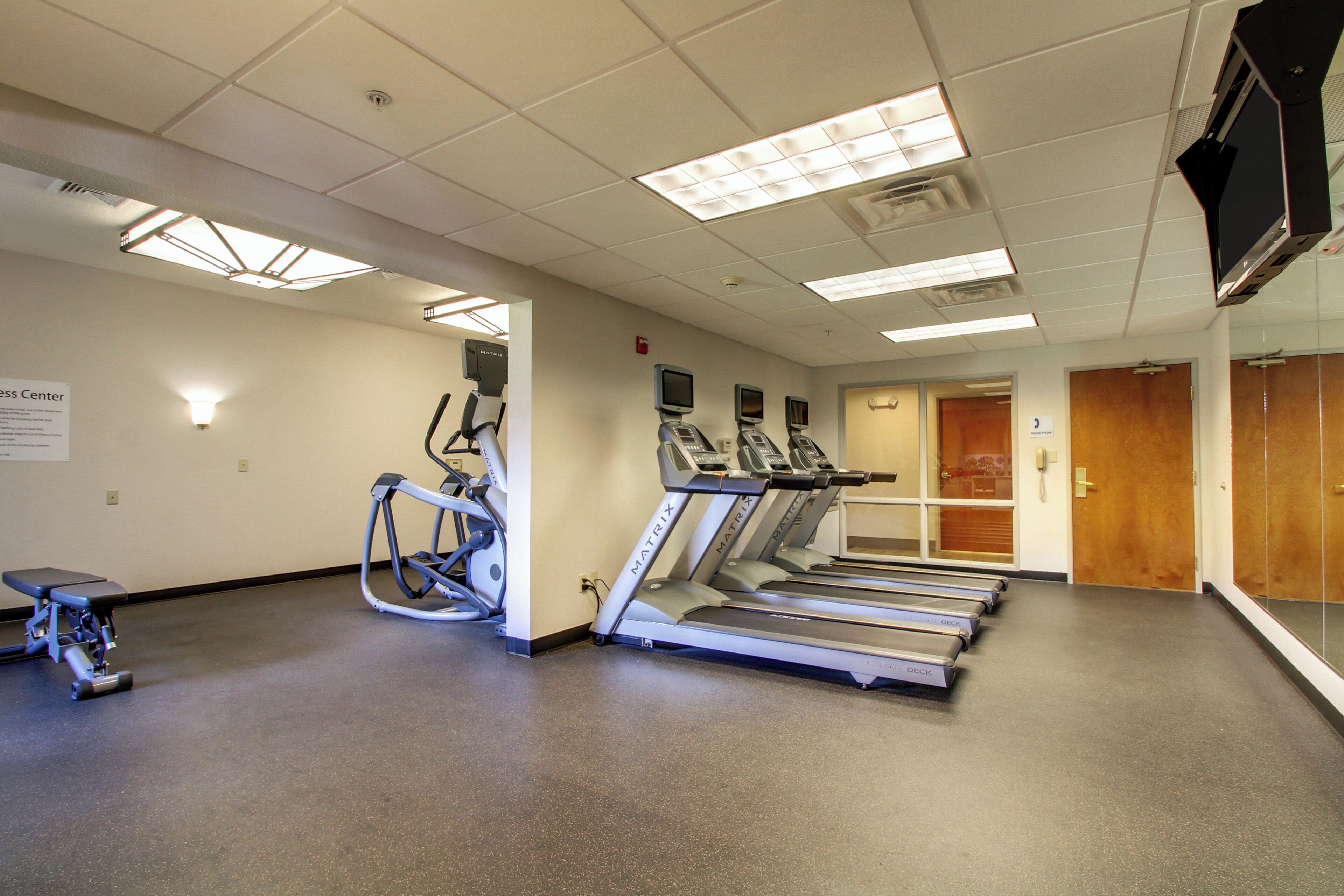 Un gimnasio con cintas de correr, una bicicleta estática y una banca.