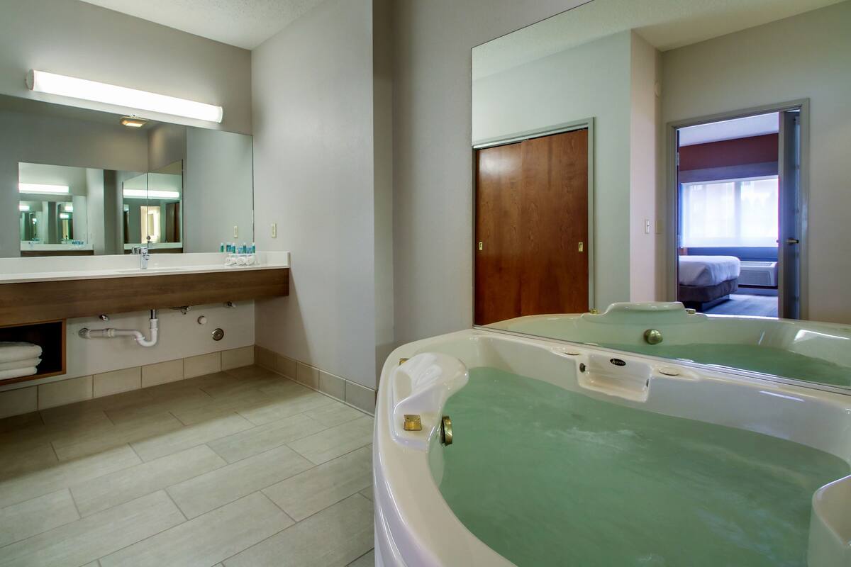 A bathroom with a large mirror, a sink with a countertop, and a bathtub with green water.