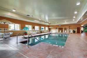 An indoor swimming pool with clear water, surrounded by lounge chairs and tables, and a tiled floor. - Holiday Inn Express Milwaukee North Brown Deer/Mequon by IHG (Milwaukee)