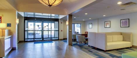 A lobby with a reception desk, a waiting area with a sofa and chairs, and a large entrance with glass doors.