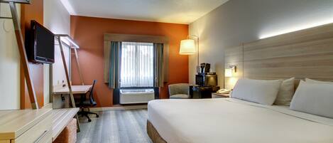 A hotel room with a bed, desk, chair, TV, and window with curtains.