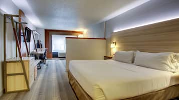 A hotel room with a large bed, a desk with a chair, a ladder, and a view of the hallway.