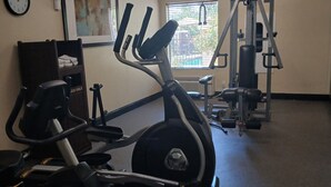 Une salle de sport équipée de machines de cardio, avec une horloge murale et une fenêtre munie de stores.