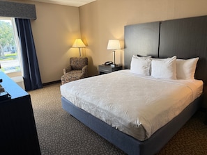 A hotel room with a large bed, two bedside lamps, a chair, a desk, and a view of the outdoors.