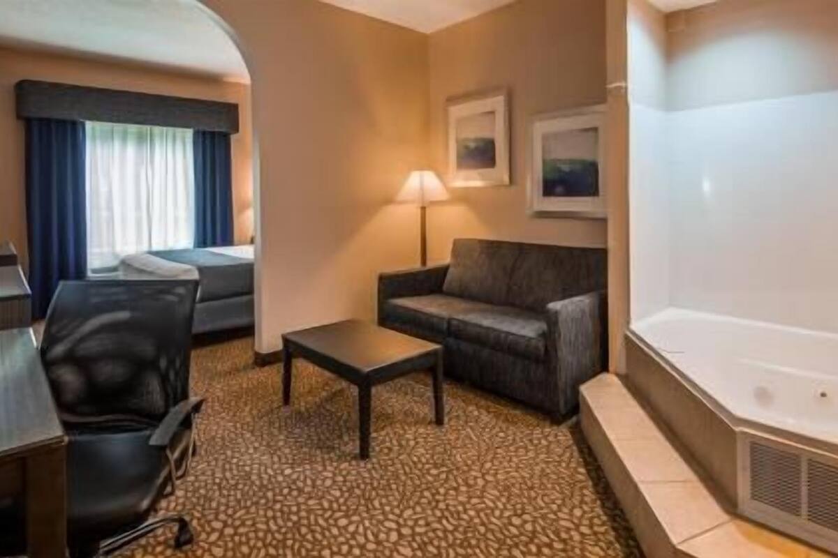 Habitación de hotel con cama, sofá, una mesita, lámpara, cuadro y bañera.