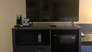 Une chambre d’hôtel compacte équipée d’un téléviseur à écran plat posé sur un meuble, d’une machine à café et d’une petite armoire avec des tiroirs.