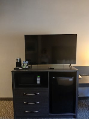 Ein kompaktes Hotelzimmer mit einem Flachbildfernseher auf einem Standfuß, einer Kaffeemaschine und einem kleinen Schrank mit Schubladen.