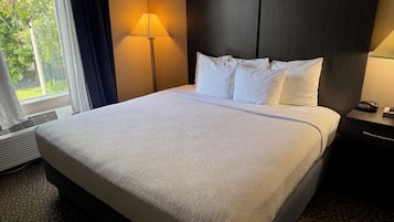 Ein Hotelzimmer mit einem Bett, einem Nachttisch mit einer Uhr und einem Fenster mit Vorhängen.