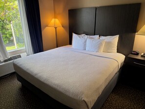 Een hotelkamer met een bed, een nachtkastje met een klok en een raam met gordijnen.