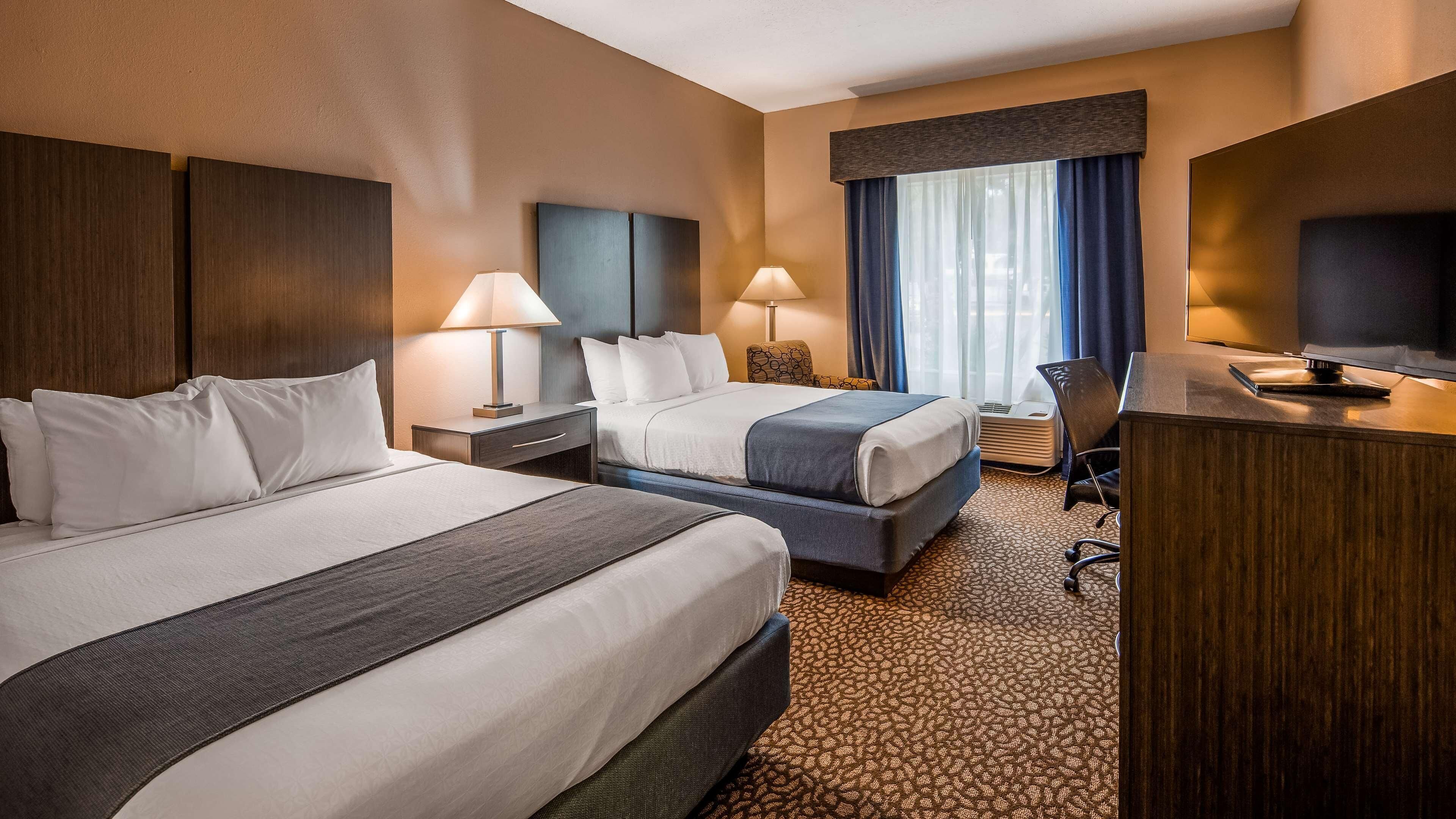 Une chambre d’hôtel avec deux lits, un bureau, une chaise, une télévision et une fenêtre avec des rideaux.