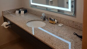 Une salle de bain moderne avec un comptoir en granit, un grand miroir doté d’un éclairage à DEL, un lavabo et un porte-serviettes.