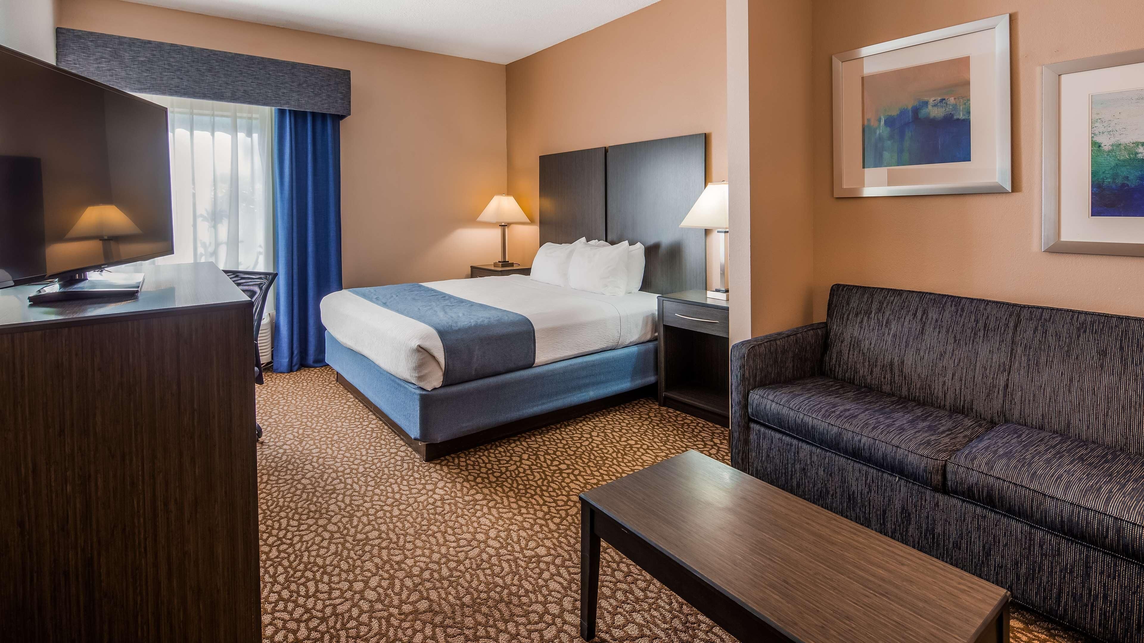 Une chambre d’hôtel comprenant un lit, deux tables de chevet, un bureau, un canapé et un téléviseur.