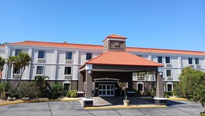 Un hôtel avec un toit recouvert de tuiles rouges, une entrée abritée et une façade symétrique dotée de nombreuses fenêtres.