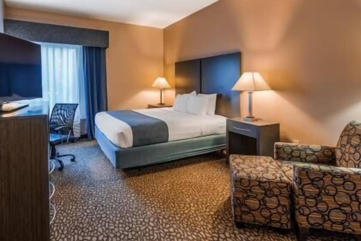 Een hotelkamer met een bed, twee bedlampen, een bureau met stoel, een televisie en een gestreept bankje.