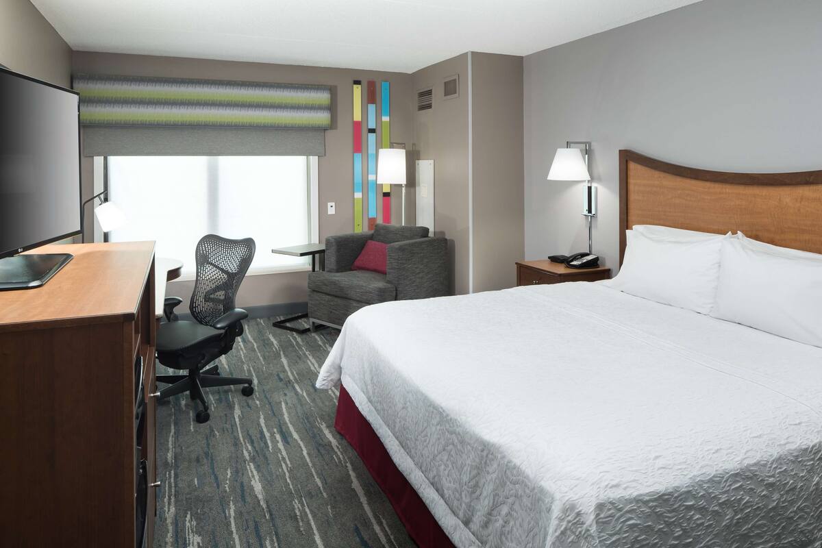A hotel room with a bed, desk, chair, and a TV.