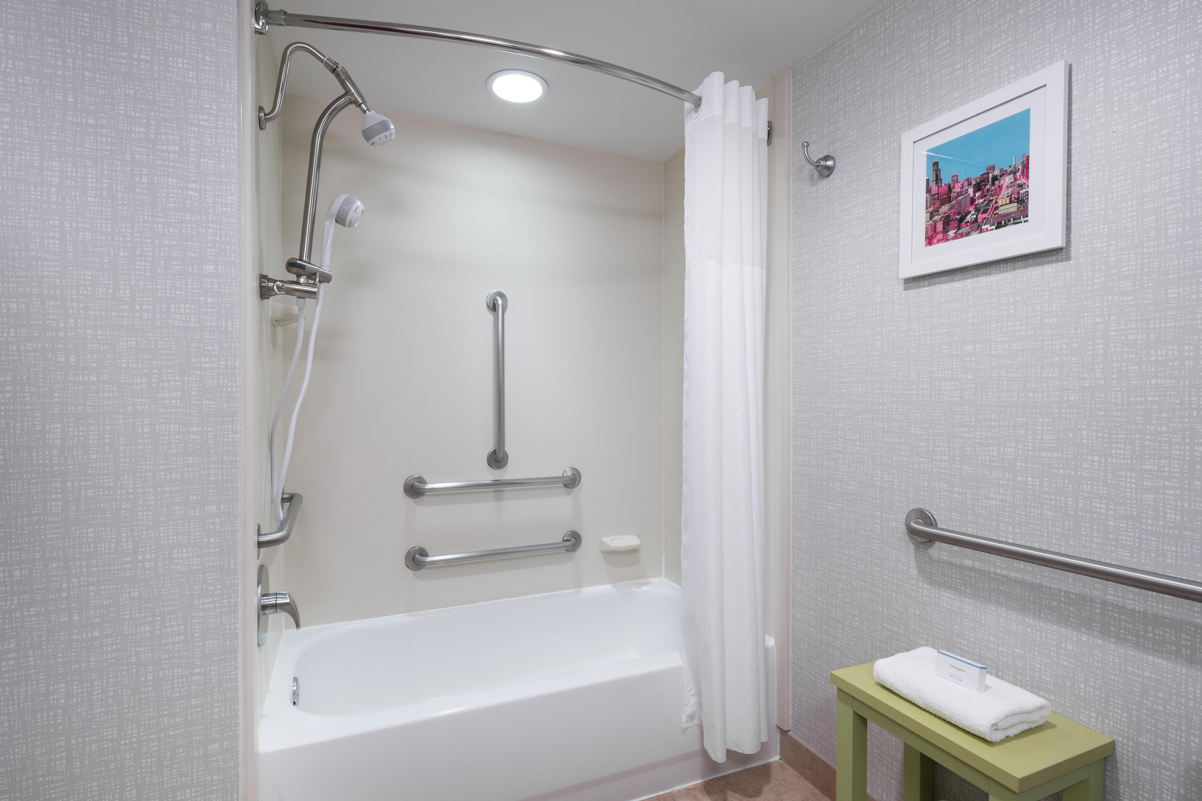 Un baño moderno con bañera, ducha, barras de apoyo, un perchero y un cuadro en la pared.