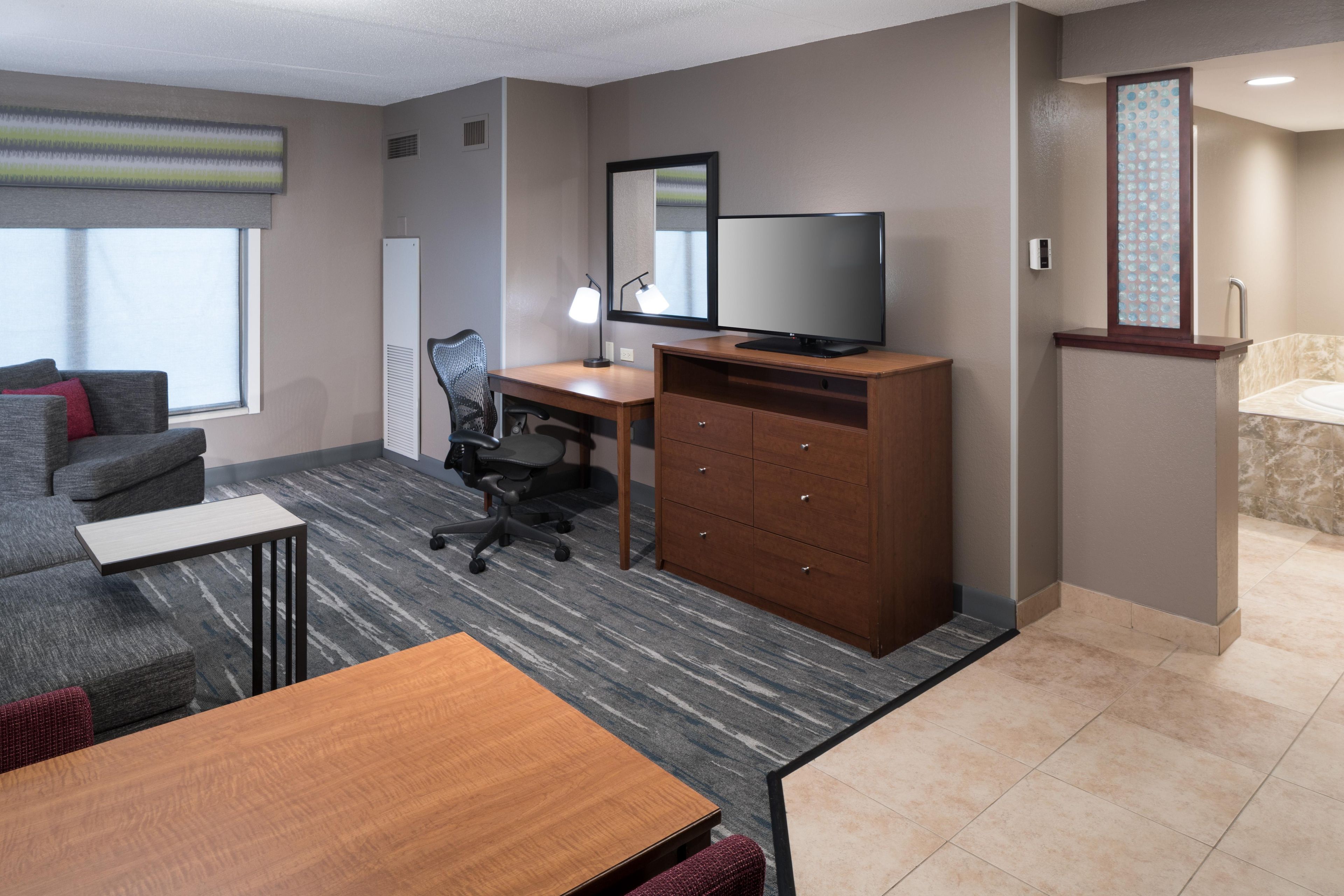 A hotel room with a sofa, a desk, a television, a dresser, and a bathroom with a bathtub.