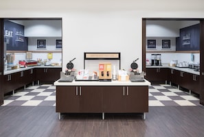 A breakfast bar with waffle makers, coffee machines, and a sign indicating breakfast starts here. - Hampton Inn & Suites Chicago-North Shore/Skokie (Skokie)