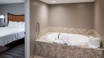 Un baño de hotel con una bañera grande, una cama con ropa blanca y un piso de baldosas de mármol.