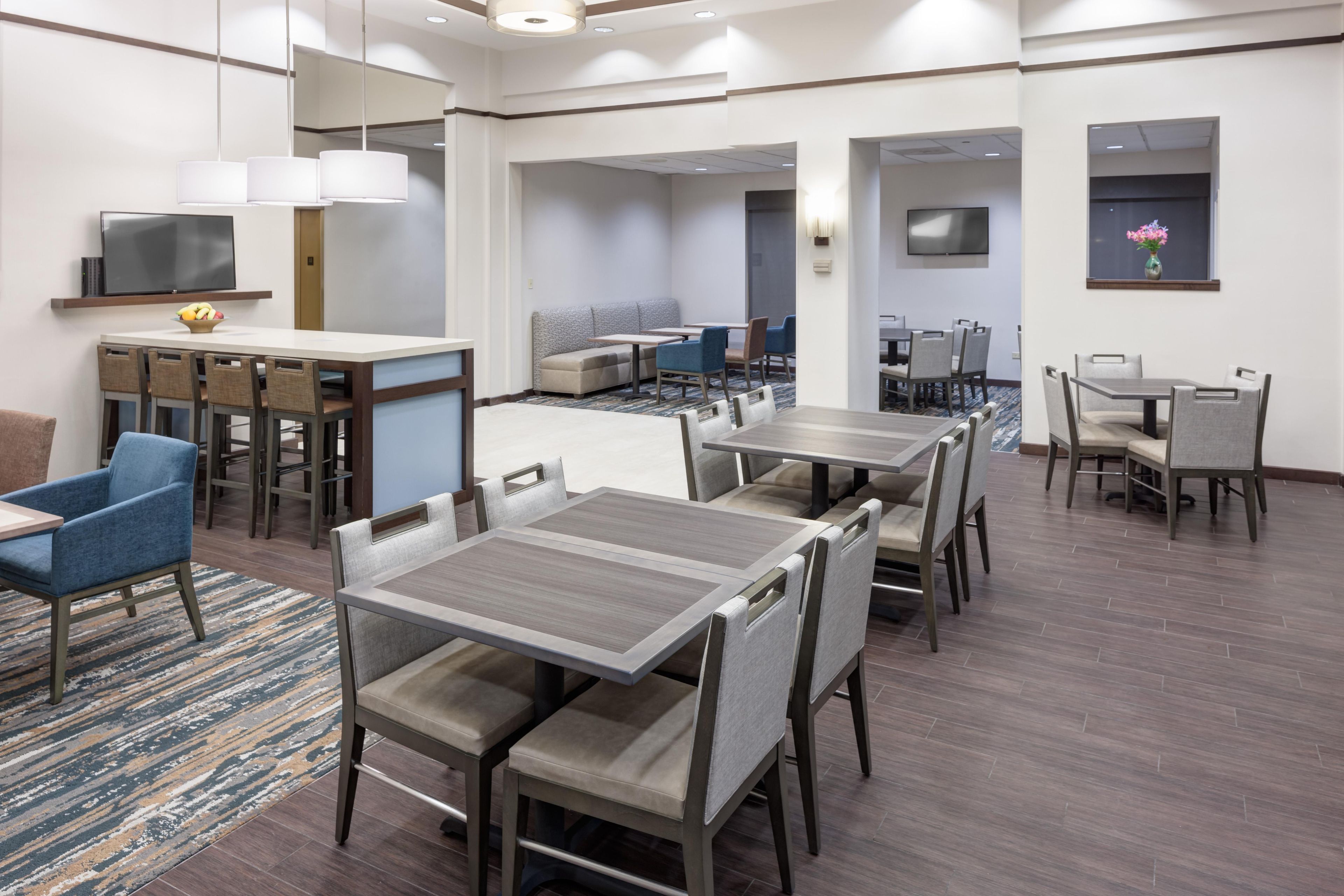 A hotel dining area with multiple tables and chairs, a television, and a seating area with sofas and a coffee table.