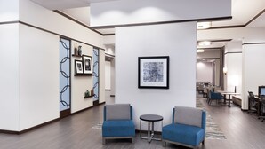Un vestíbulo moderno con dos sillones azules, una mesita redonda y una obra de arte abstracta enmarcada en la pared.