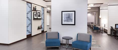 Um hall moderno com duas poltronas azuis, uma mesinha redonda e uma obra de arte abstrata emoldurada na parede.