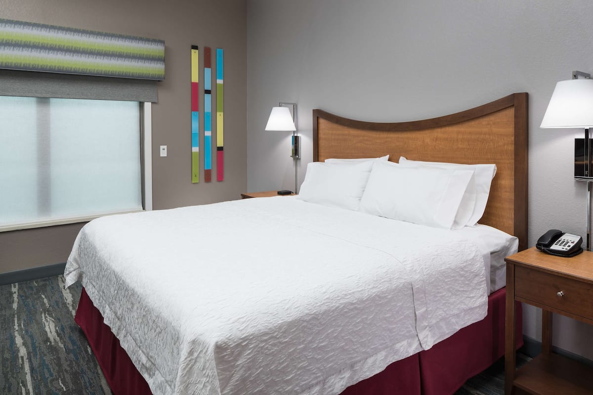 A neatly made bed with white linens, a wooden headboard, and a bedside table with a lamp and a phone.