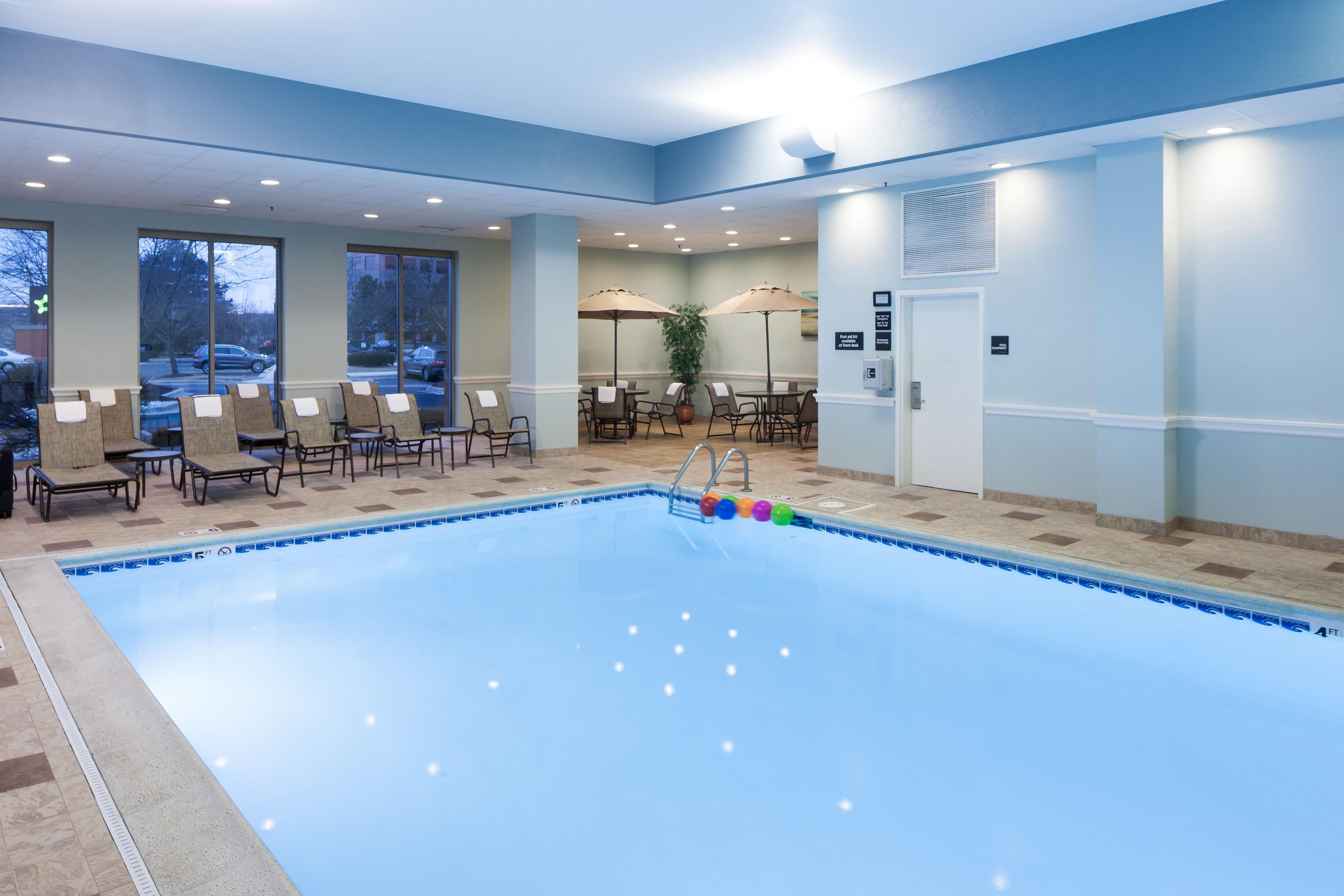 Un espace piscine d’hôtel avec des chaises longues et des parasols, une piscine dont la profondeur est indiquée, et une porte avec une pancarte.