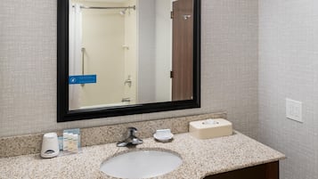 A bathroom with a granite countertop, a sink, a mirror, and a towel dispenser.