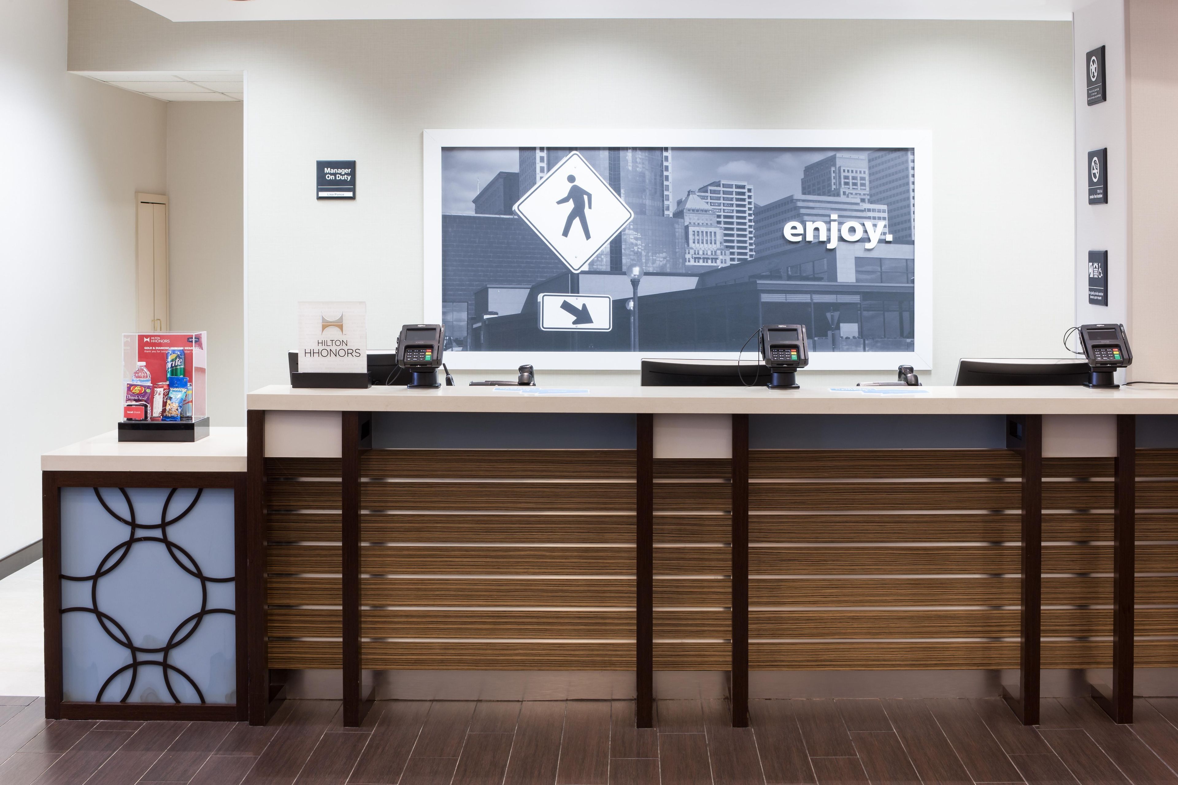 A hotel reception desk with a large digital display, multiple card readers, and a 'Manager On Duty' sign.