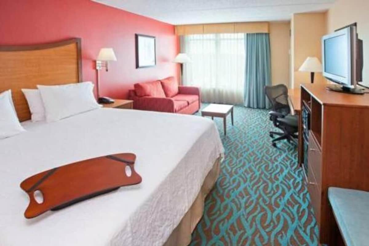 A hotel room with a bed, a desk, a chair, a television, and a window with curtains.