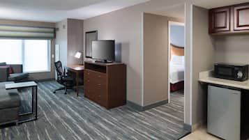 Una habitación de hotel con escritorio, silla, televisor, minibar y vista a la cama.