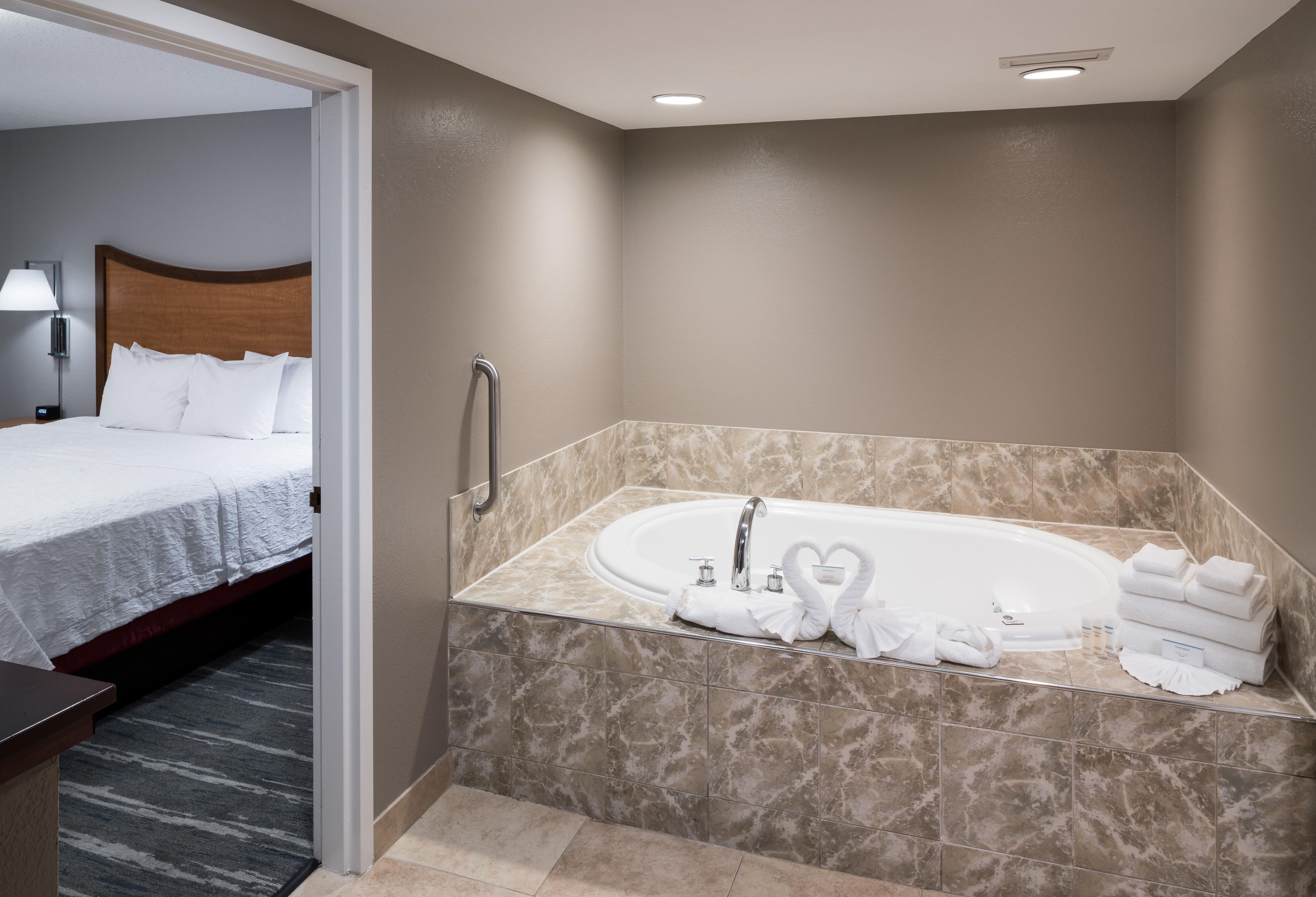 A hotel room with a large bathtub, a bed, and a bathroom with marble tiles.
