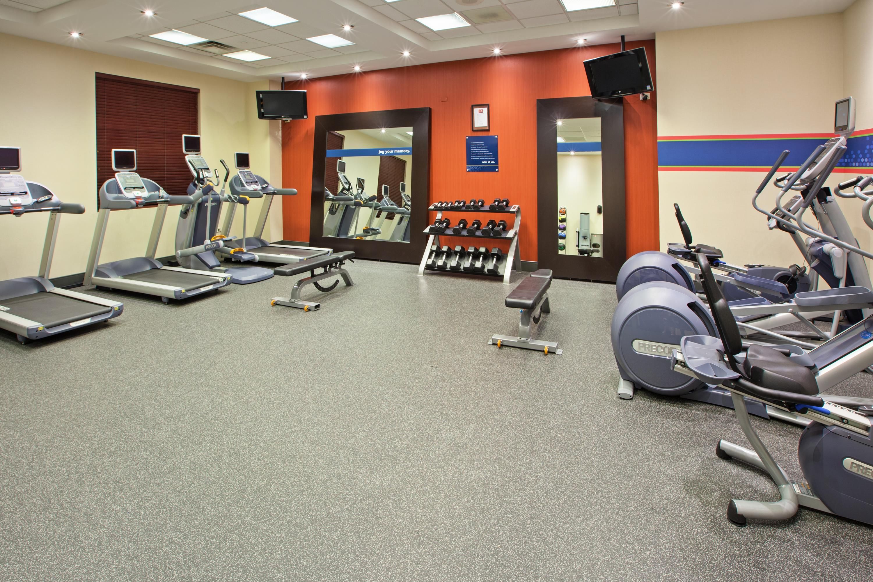 Un centre de remise en forme équipé de tapis de course, de vélos elliptiques et d’un banc de musculation.