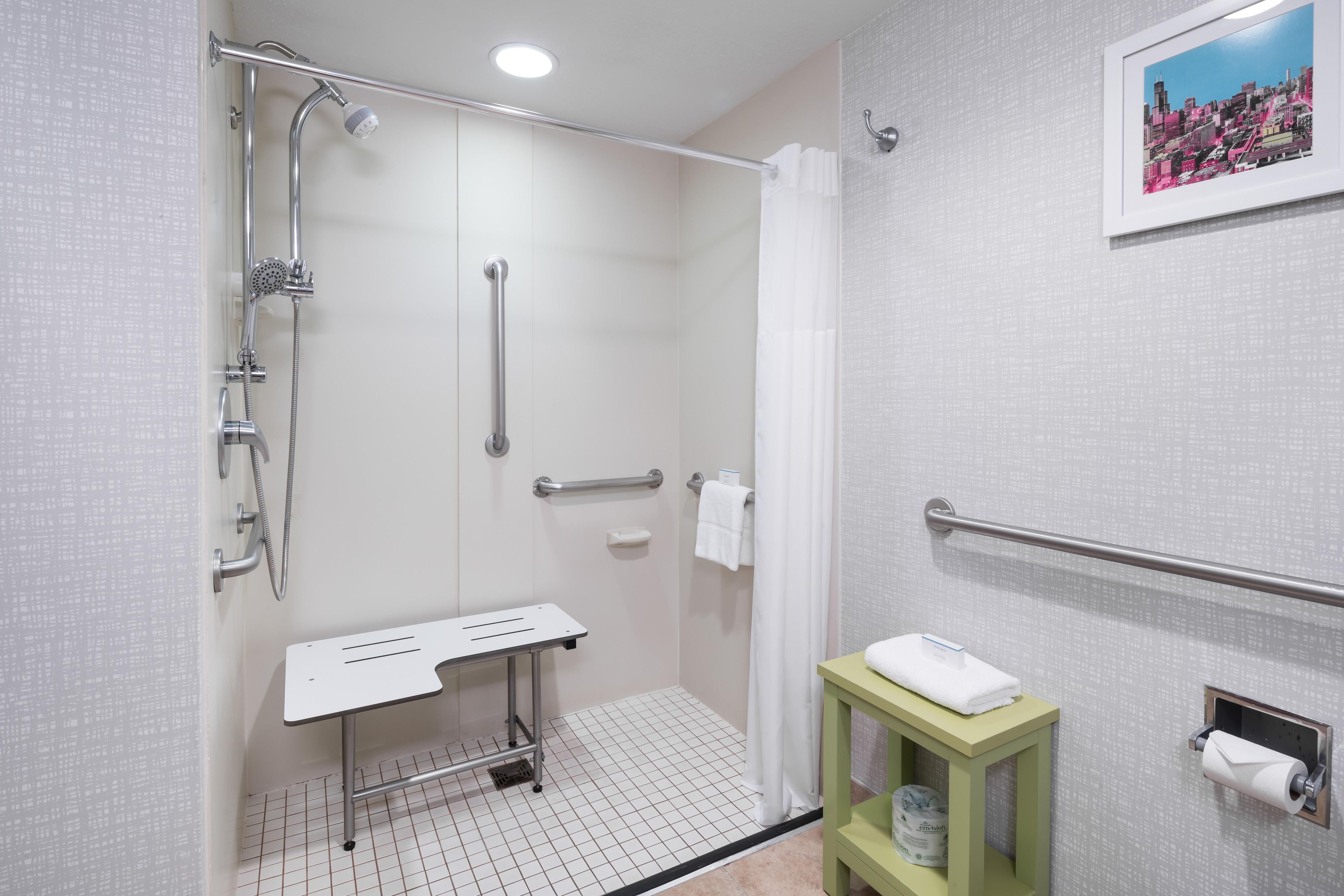 A bathroom with a shower, grab bars, a towel rack, and a toilet paper holder.