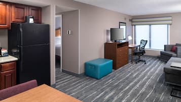 Quarto de hotel com cozinha compacta, televisão, secretária, cadeira, sofá e janela com cortinas.