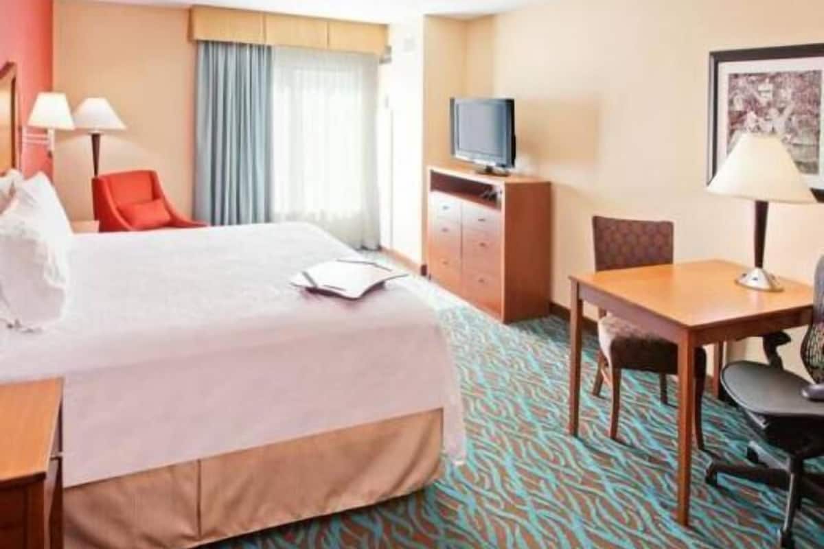 A hotel room with a bed, a desk, a chair, a television, and a wardrobe.