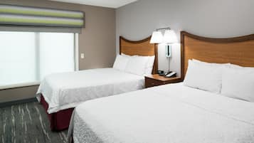 A hotel room with two beds, a nightstand with a lamp, and a window with blinds.