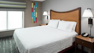 Una habitación de hotel con una cama grande, dos mesitas de noche con lámparas, un teléfono en la pared y una ventana con persianas.