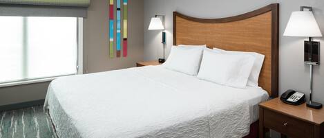 A hotel room with a large bed, two bedside tables with lamps, a wall-mounted phone, and a window with blinds.