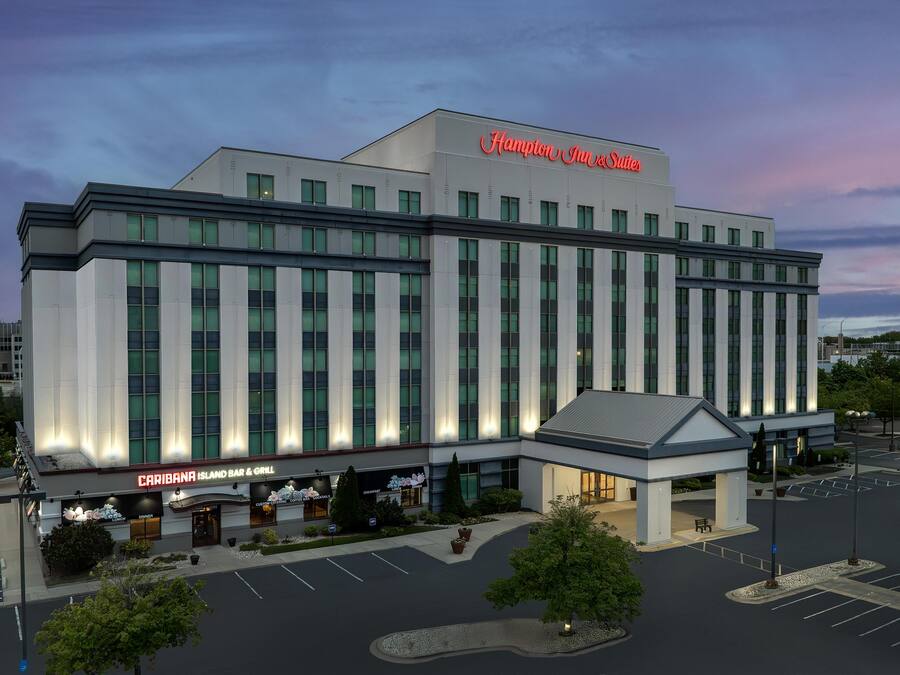 Ein großes Hotel mit einem gut sichtbaren Hampton Inn & Suites Schild, einer Caribana Island Bar & Grill und einem Parkplatz.