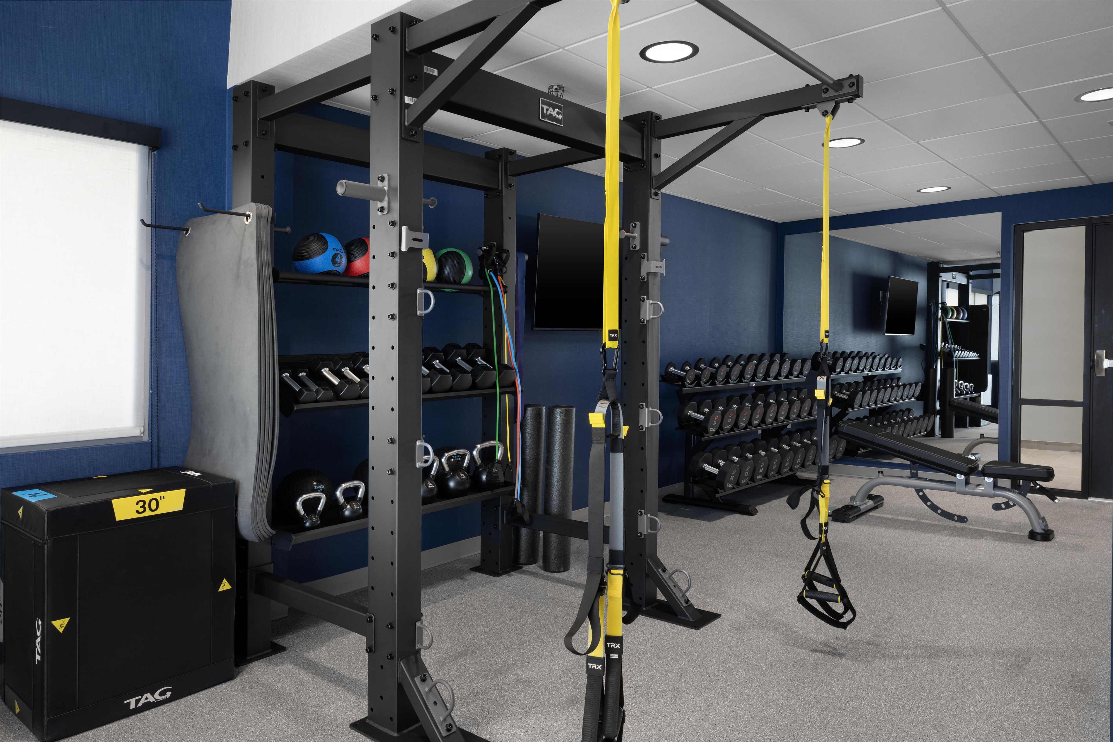 A gym with weightlifting equipment, dumbbells, and TRX suspension trainers.