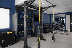 Un gimnasio con equipo de levantamiento de pesas, mancuernas y entrenadores TRX de suspensión.