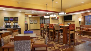 A hotel dining area with multiple tables and chairs, a television mounted on the wall, and a coffee station. - Hampton Inn Dry Ridge (Dry Ridge)