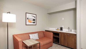 A compact hotel room with a sofa, a small table, a lamp, a framed abstract artwork, and a kitchenette. - Hampton Inn Dry Ridge (Dry Ridge)