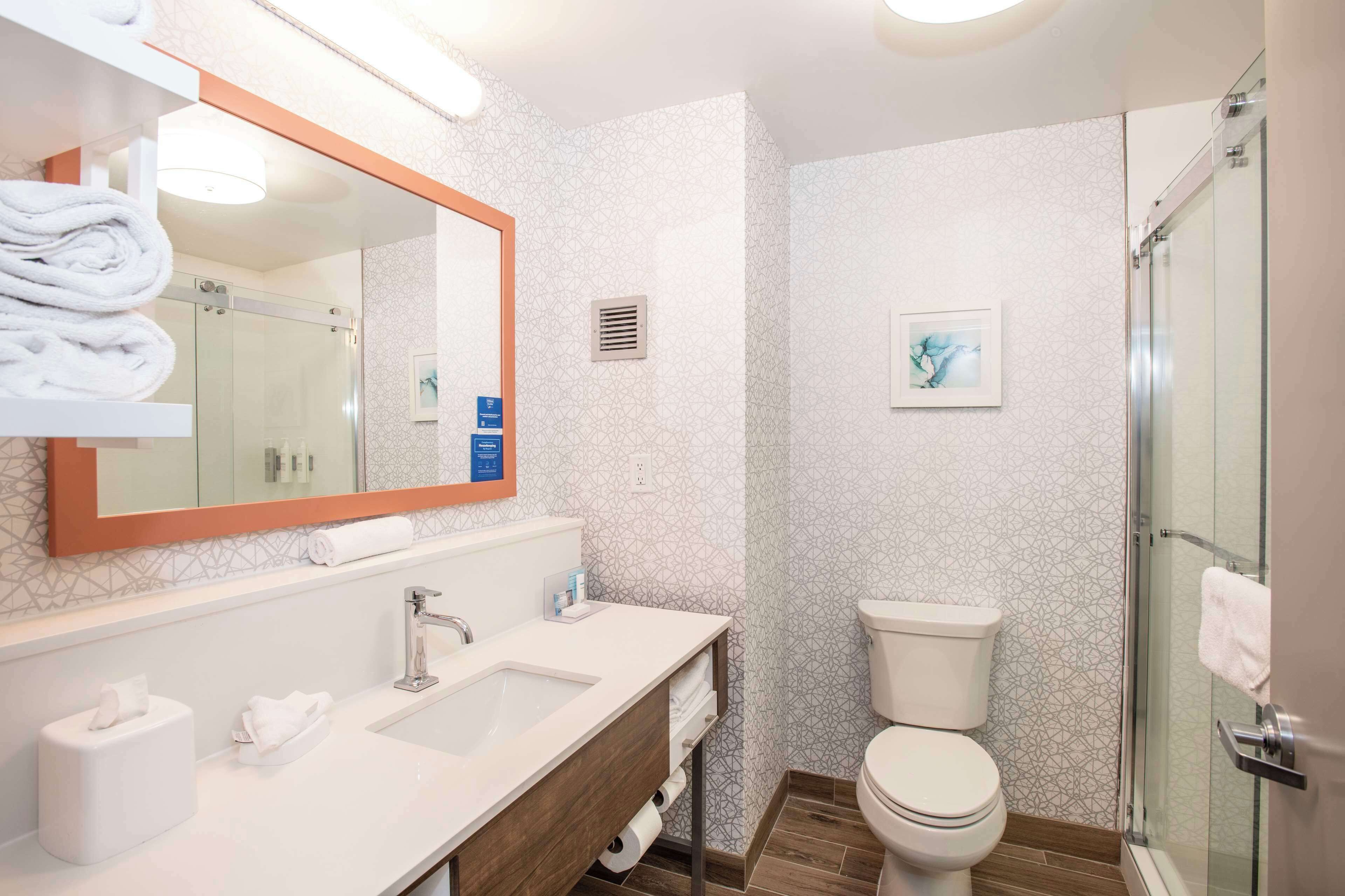 A modern bathroom with a large mirror, a sink, a toilet, and a glass-enclosed shower.