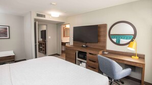 Hotellihuone, jossa on sänky, työpöytä tietokoneella, televisio, peili ja lamppu.