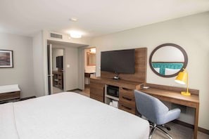 Quarto de hotel com cama, escrivaninha com computador, televisão, espelho e abajur.