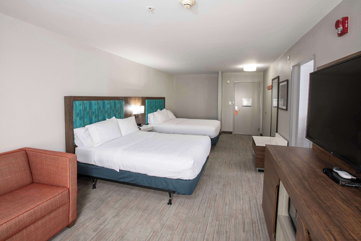 A hotel room with two beds, a TV, a desk, and a red sofa.